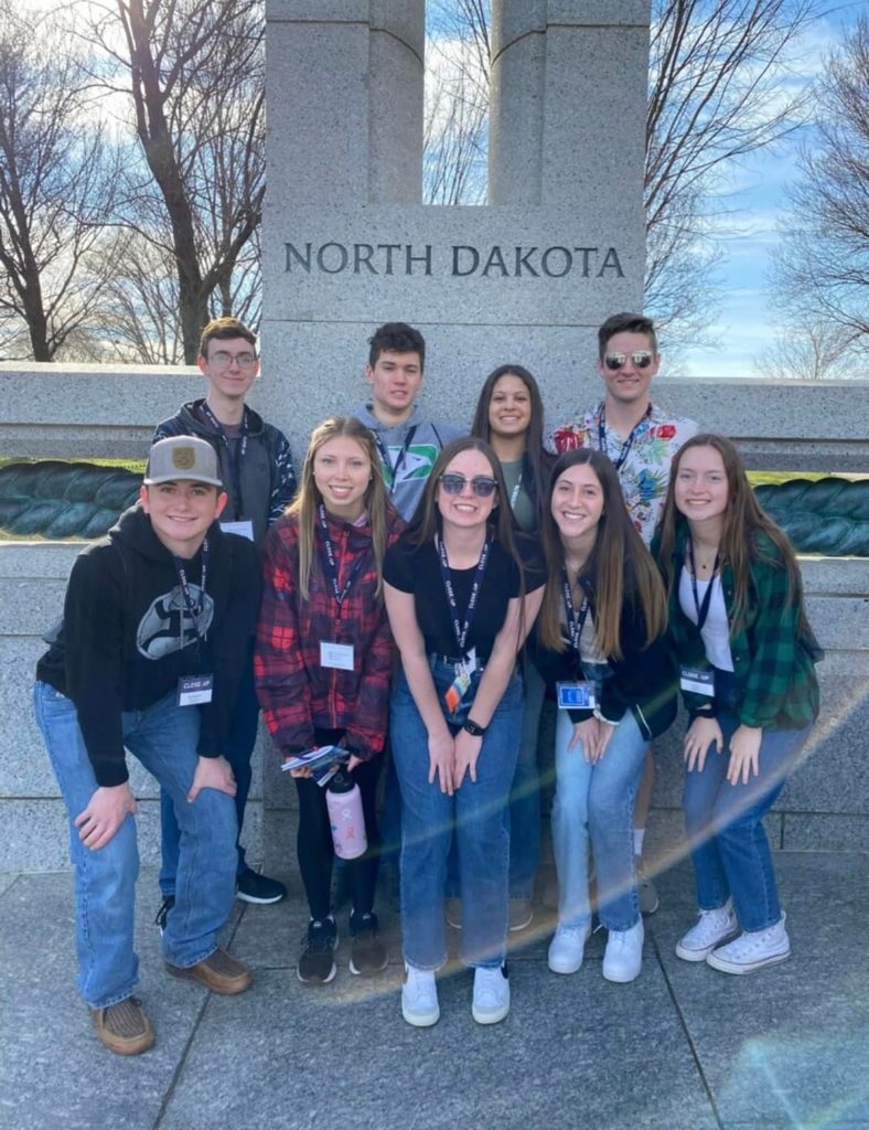 student group in front of stone wall with north dakota ingraved in