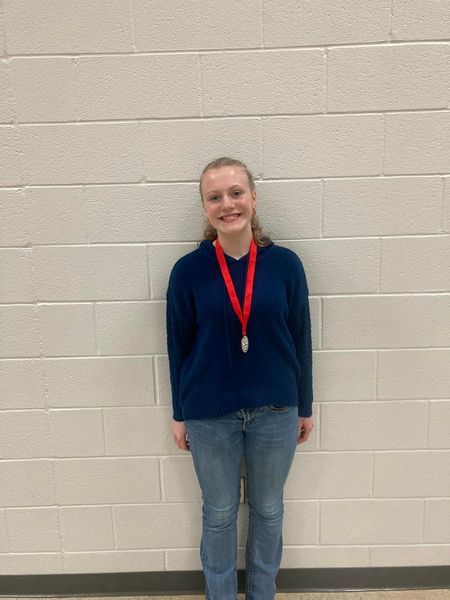 Student at county math meet wearing red ribbon medal posing in front of white brick wall